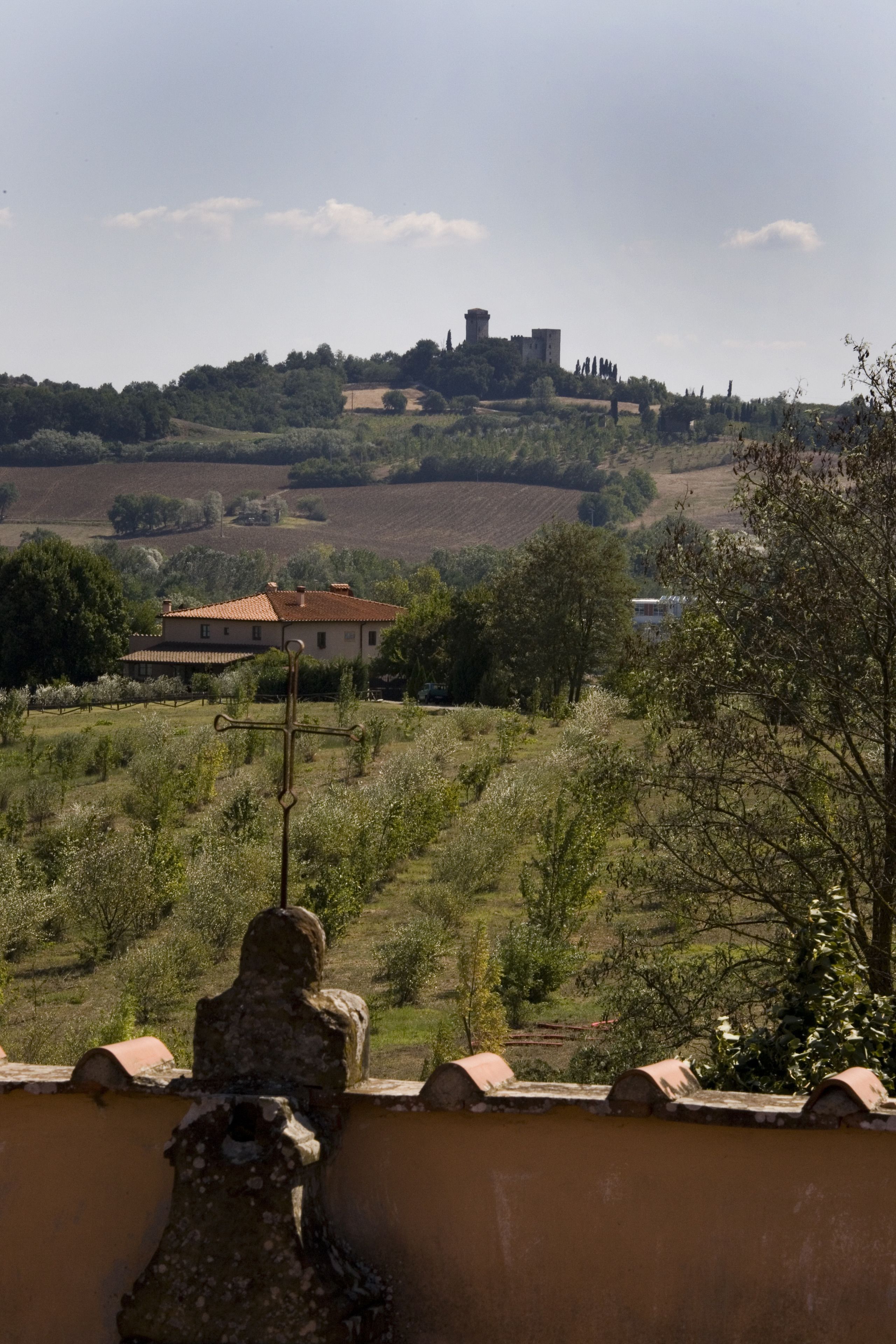 A rural landscape with a stone wall, a cross, and a distant castle on a hill.