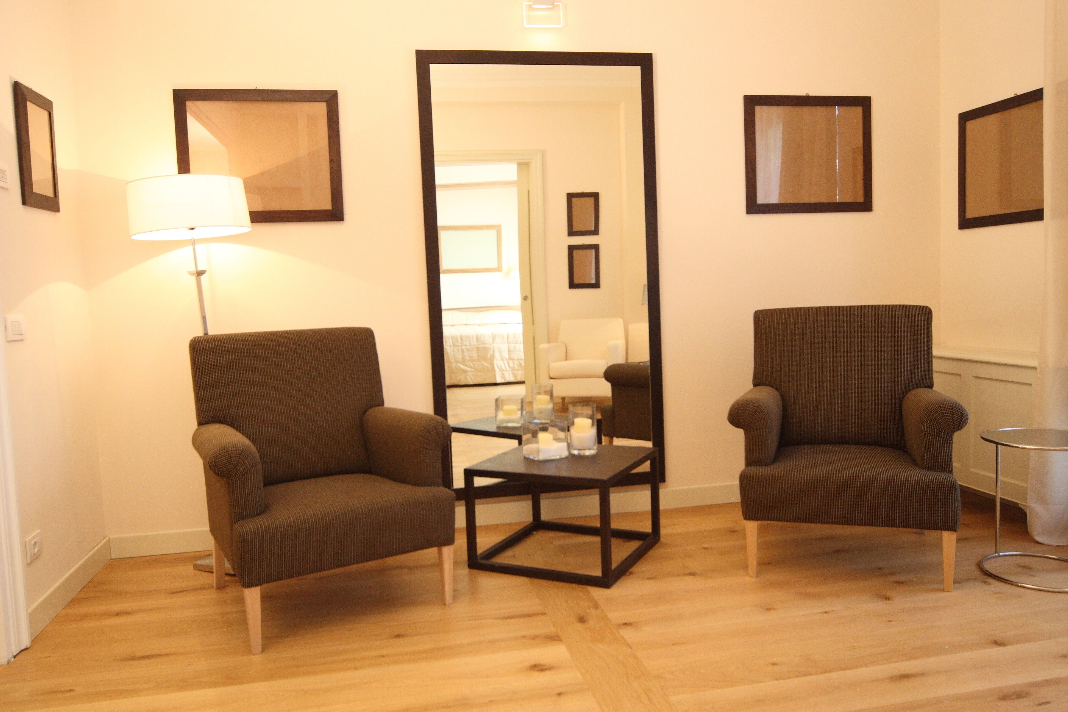Une pièce avec deux fauteuils marron, une petite table avec des bougies et un miroir au mur.