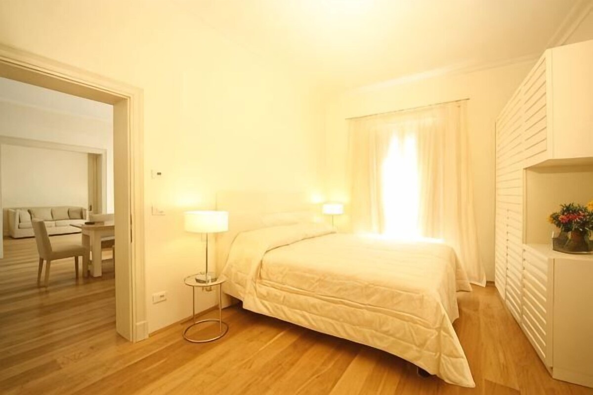 Une chambre d’hôtel avec un lit, des lampes de chevet, une petite table, une chaise et une vue sur un balcon.