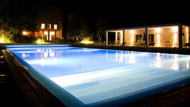 Piscina com superfície de água azul translúcida, rodeada por um deck bem iluminado com área de estar ao ar livre.