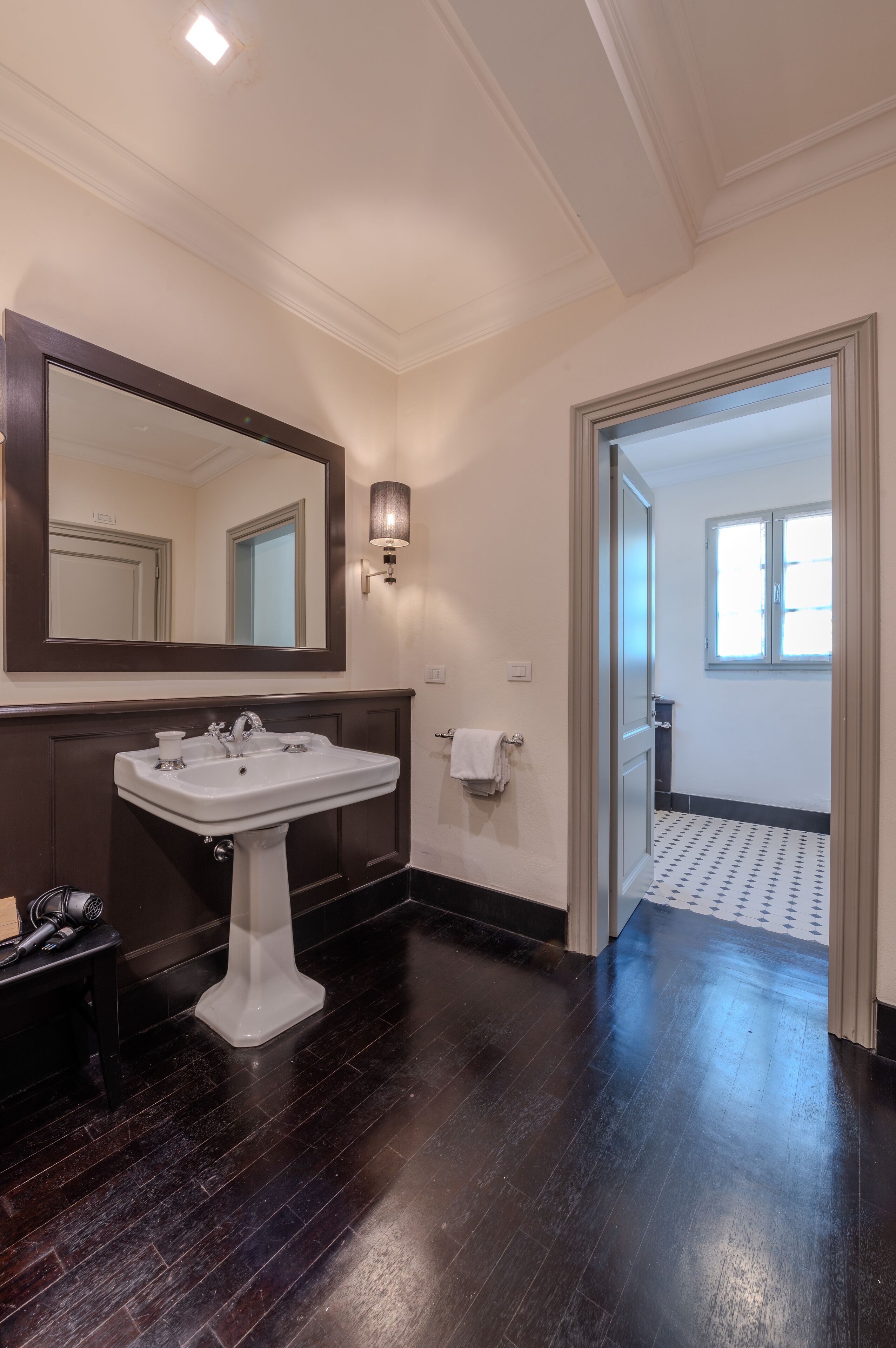 A bathroom with a white pedestal sink, a large mirror, and a wall-mounted light fixture.