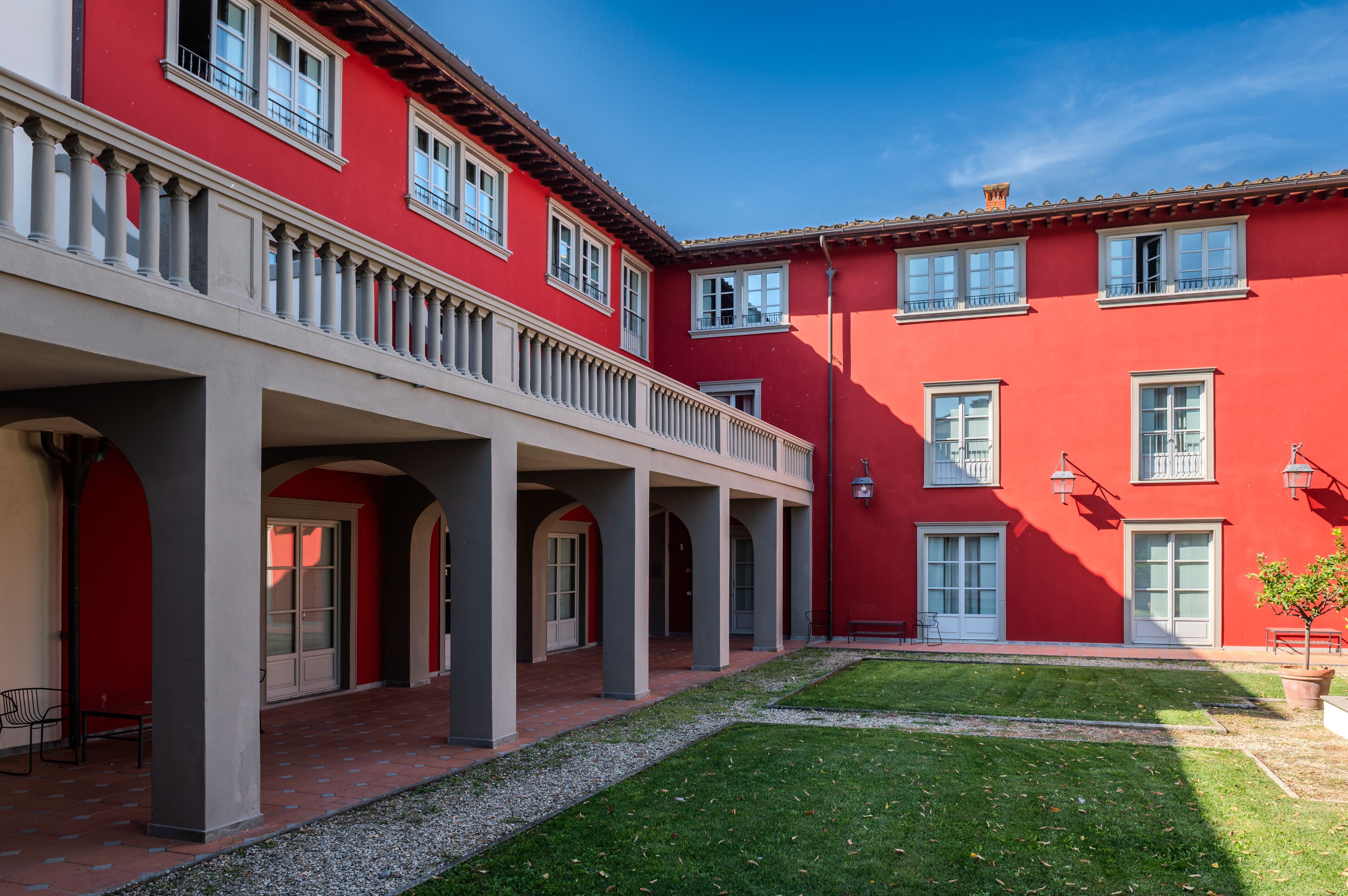 A courtyard with a red building, covered walkway, and a small lawn area.