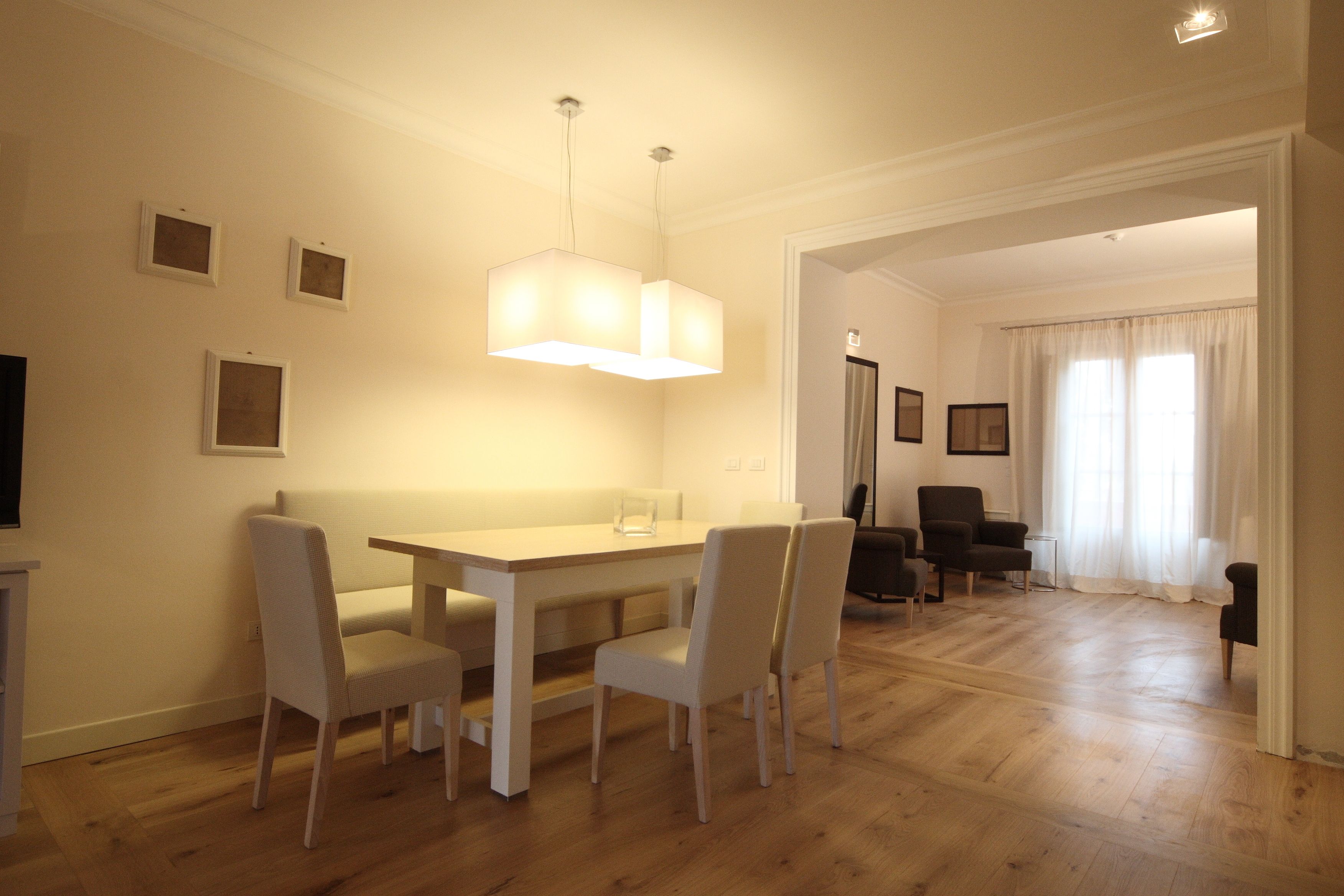 Un coin repas avec une table et des chaises en bois, un luminaire suspendu et une vue sur une autre pièce où se trouvent une chaise et une table.