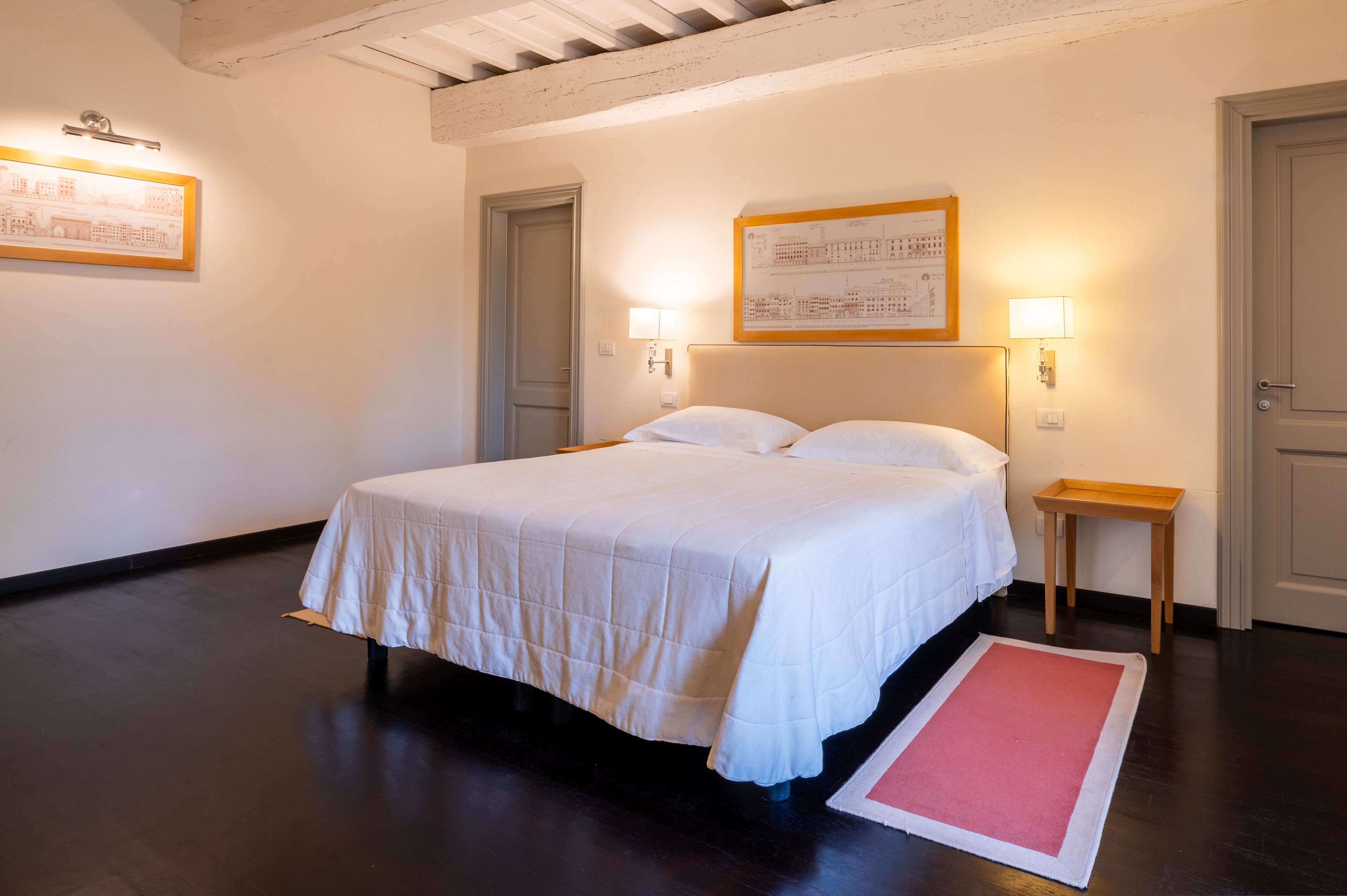 Une chambre d’hôtel avec un lit, deux lampes de chevet, une petite table de nuit en bois et un tapis rouge.