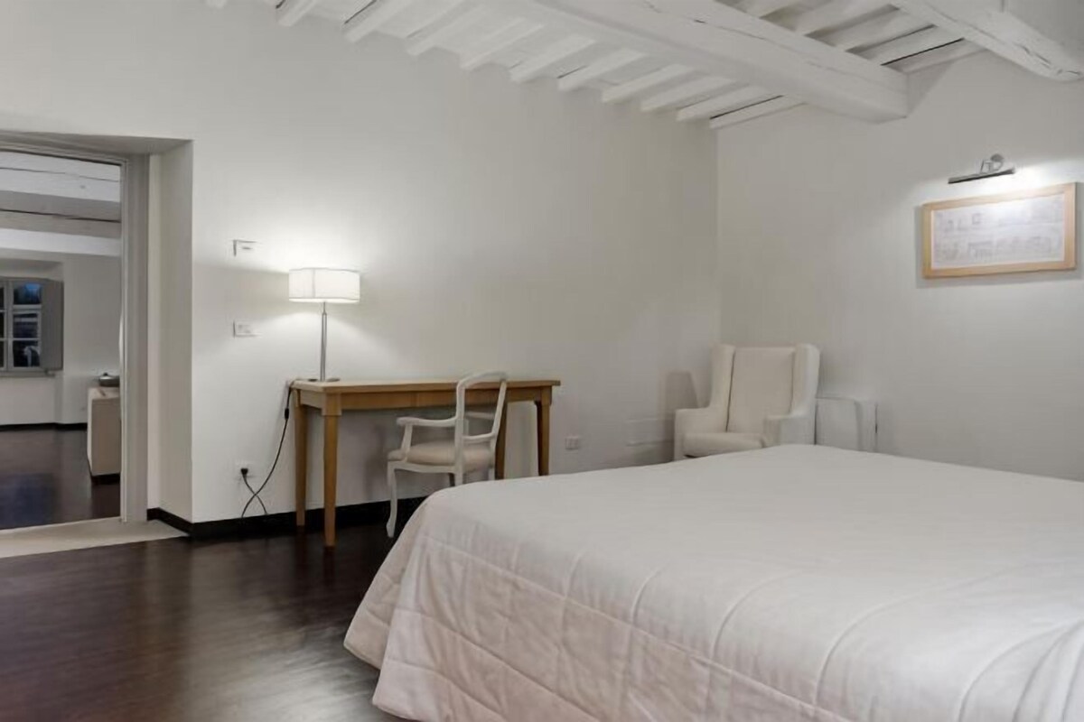 Une chambre d’hôtel avec un lit, un bureau, deux chaises, une lampe et un certificat encadré accroché au mur.