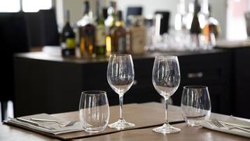 A table set with three wine glasses and cutlery, with bottles in the background.