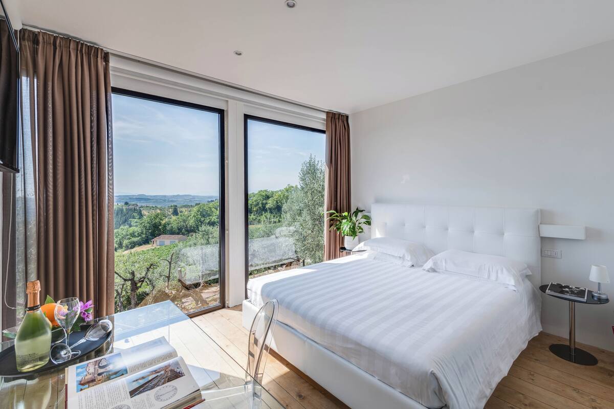 Habitación de hotel moderna con una cama grande, un escritorio con ordenador y vistas a un viñedo.