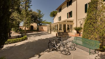Un patio con un sendero de piedra, un banco verde y bicicletas estacionadas cerca de un edificio con cerramiento de vidrio.