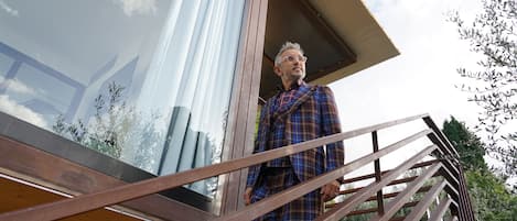 A person standing on a wooden deck with a metal railing, overlooking a modern building with large windows and a view of the sky.