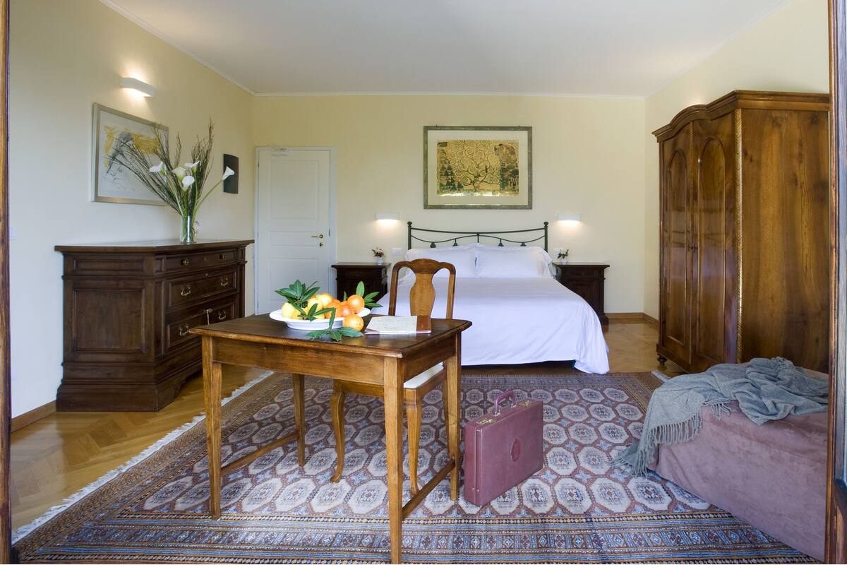 Un dormitorio con cama, mesitas de noche, cómoda de madera, una mesa con fruta y un tapete estampado.