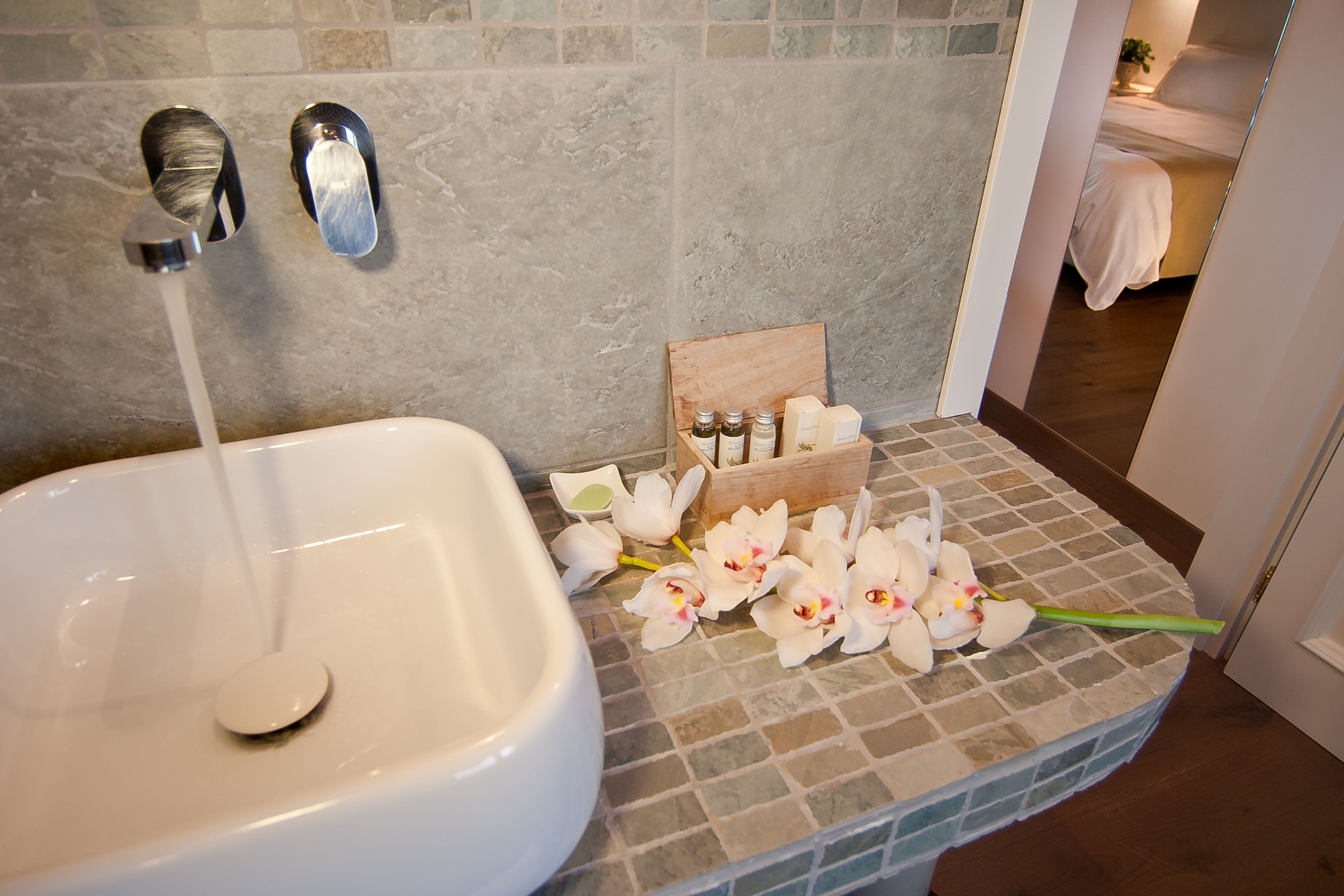 Un baño con lavamanos blanco, dos grifos y una caja de madera con artículos de aseo.