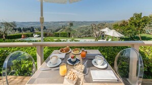 Una mesa con alimentos para desayuno, una vista despejada del campo y un paraguas blanco.
