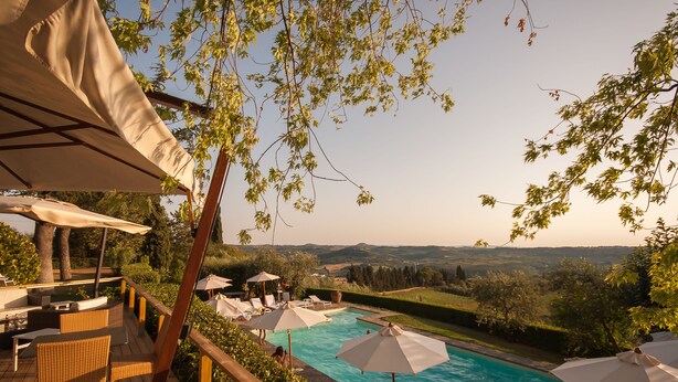 Zona de piscina con mobiliario exterior y sombrillas, con vistas a un paisaje pintoresco.