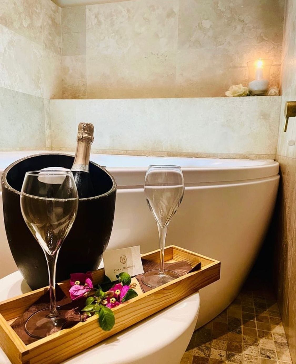 Un baño con una bañera, una botella de champán y dos copas de vino sobre una bandeja con flores.