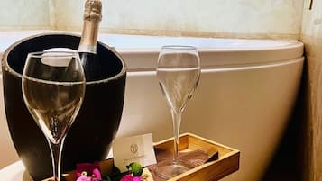 Un baño con una bañera, una botella de champán y dos copas de vino sobre una bandeja con flores.