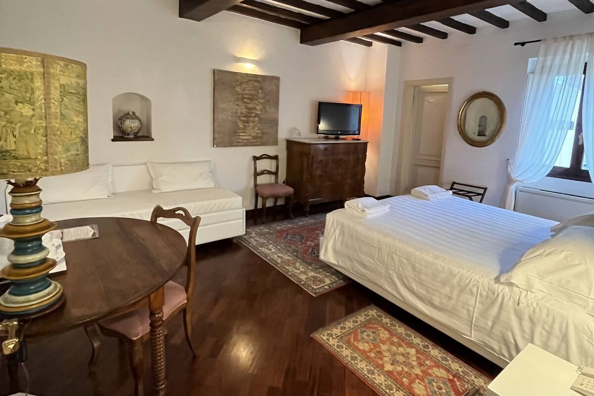 Una habitación con cama, televisión, sofá, mesa de comedor y candelabro.