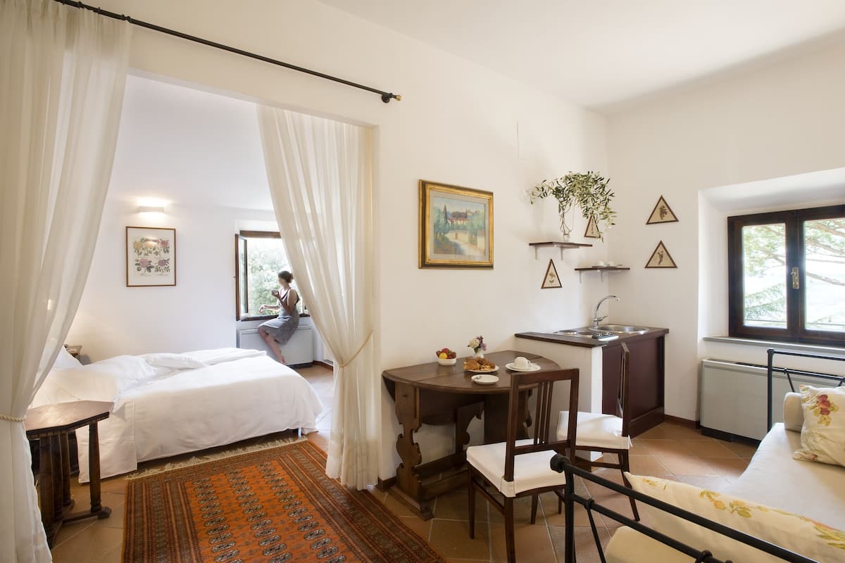 Un dormitorio con dos camas, una mesa de comedor, una silla, una pequeña cocina y un ventanal.