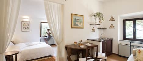 A bedroom with two beds, a dining table, a chair, a small kitchen area, and a window.