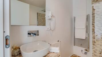 Un bagno con un lavandino ovale grande, un porta asciugamani, uno specchio e una zona doccia con parete piastrellata.