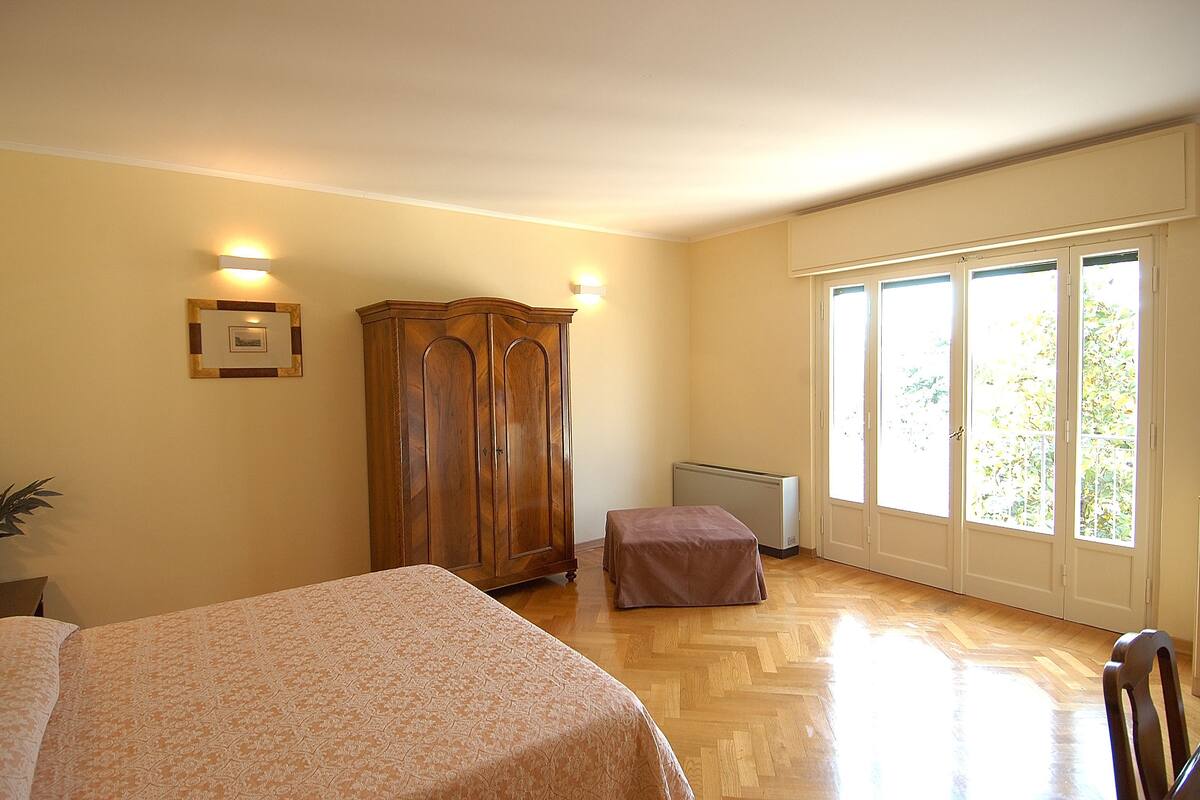 Un dormitorio con cama, un armario de madera, un radiador y una ventana con vistas a zonas verdes.