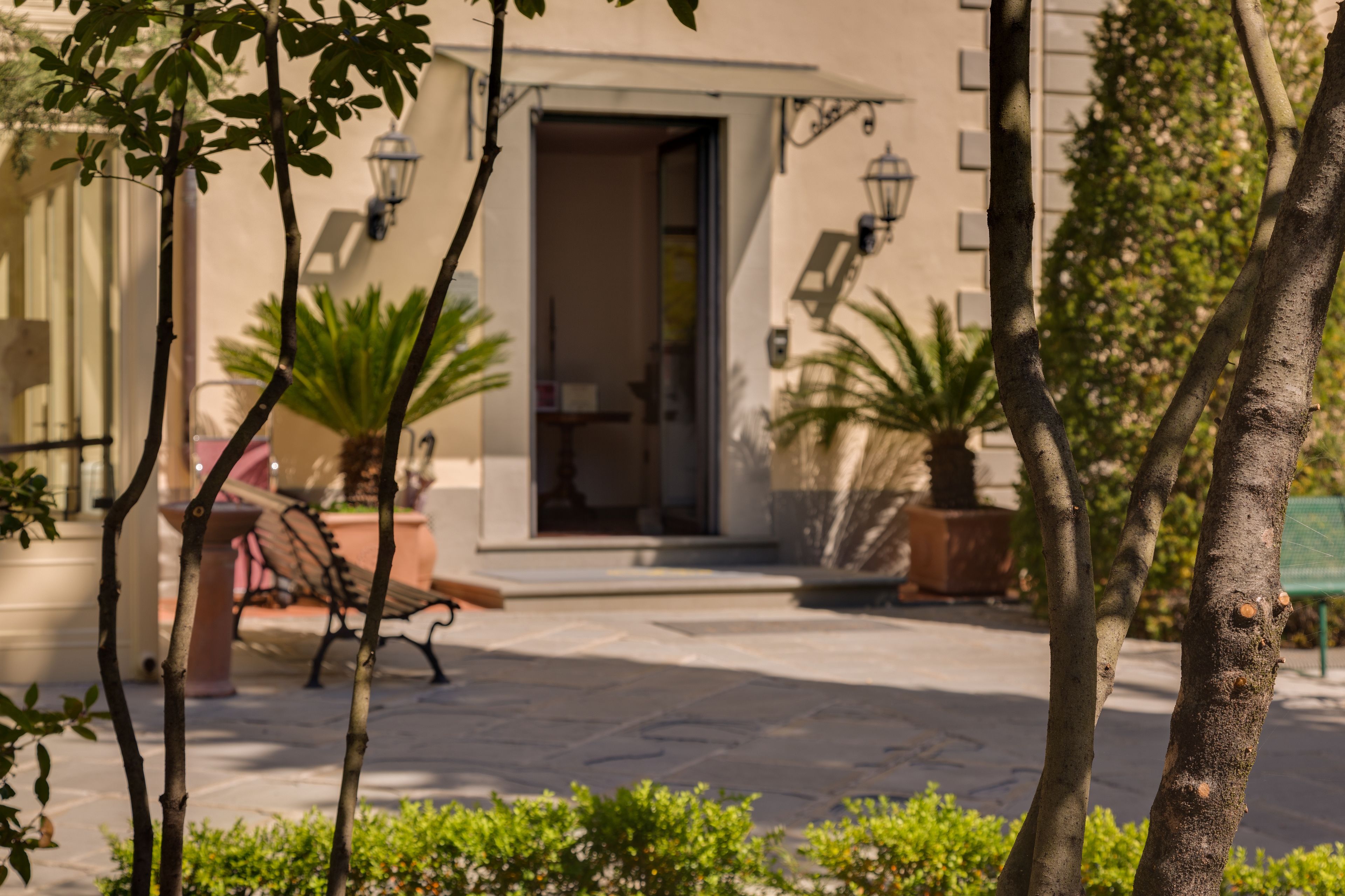 A courtyard with a stone floor, a bench, and potted plants.