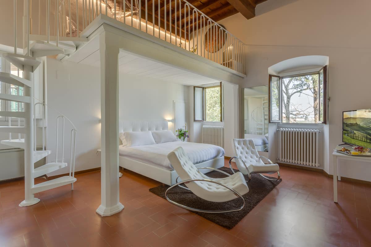 Un dormitorio moderno con cama, muebles blancos, una escalera y un ventanal grande.