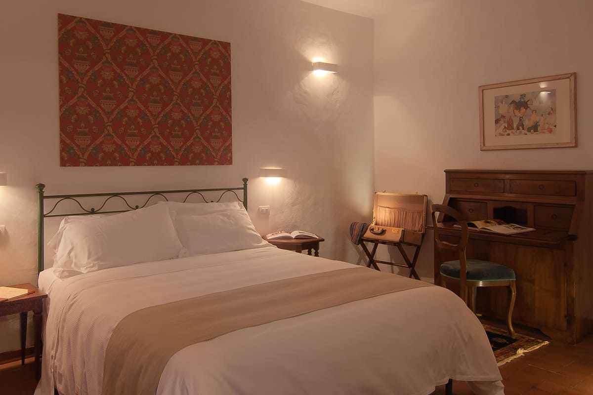 Una cama bien hecha con ropa blanca, un tapiz decorativo y un escritorio con una silla.