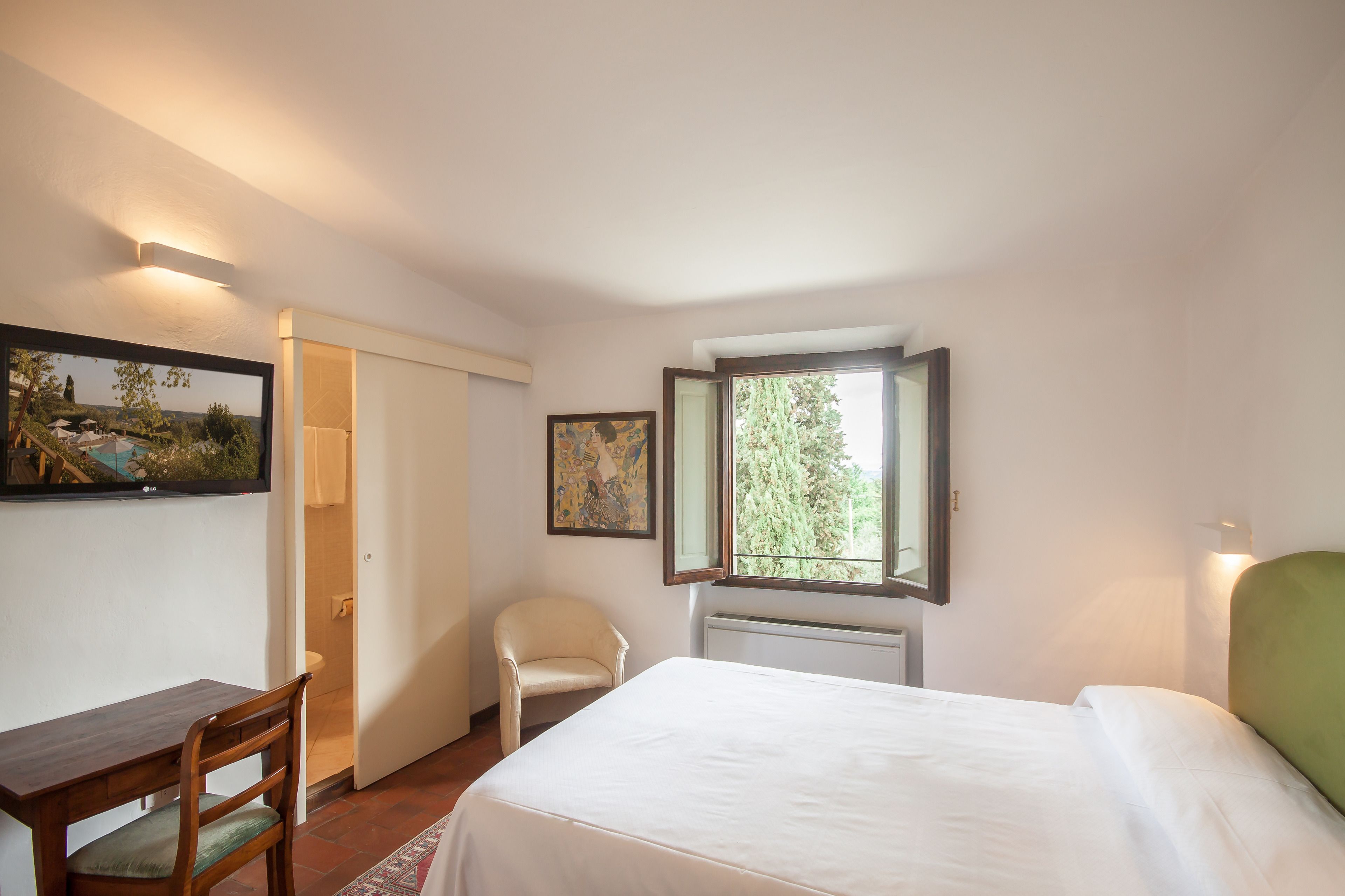 A bedroom with a bed, a chair, a table, a window, and a painting on the wall.