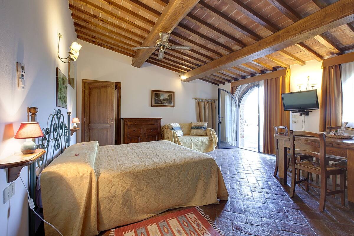 Una habitación con dos camas, techo de madera, televisión y ventana con cortinas.