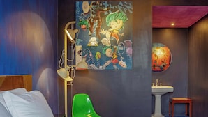 Un dormitorio con una cama, un sillón verde, una lámpara de pared, un cuadro y un lavabo.