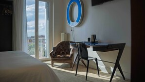 Habitación de hotel con cama, escritorio, silla, televisión y balcón con vistas.