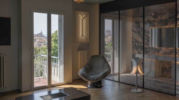 Un interior moderno con un gran ventanal corredera, una silla original y un panel decorativo en la pared.