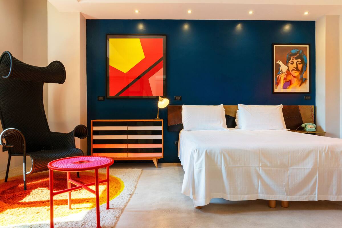 A modern bedroom with a bed, a chair, a small table, and artwork on the walls.