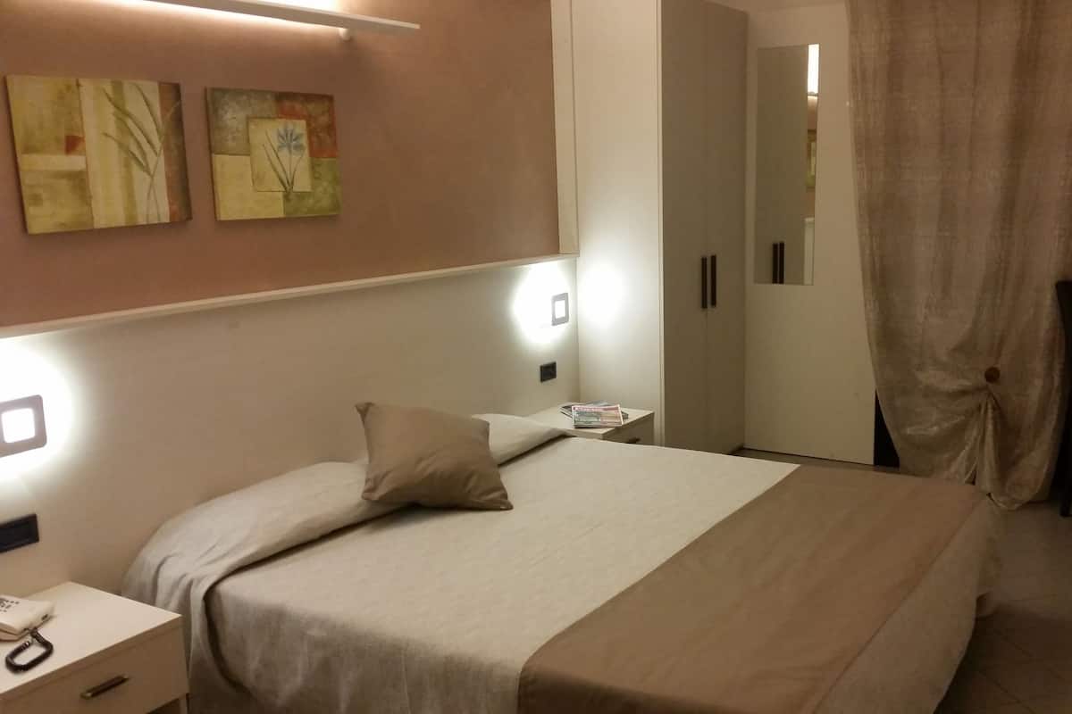 Habitación de hotel con cama, mesitas de noche, escritorio, silla, armario y cortina.