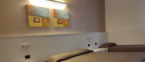 A hotel room with two beds, a nightstand, a lamp, and artwork on the wall.