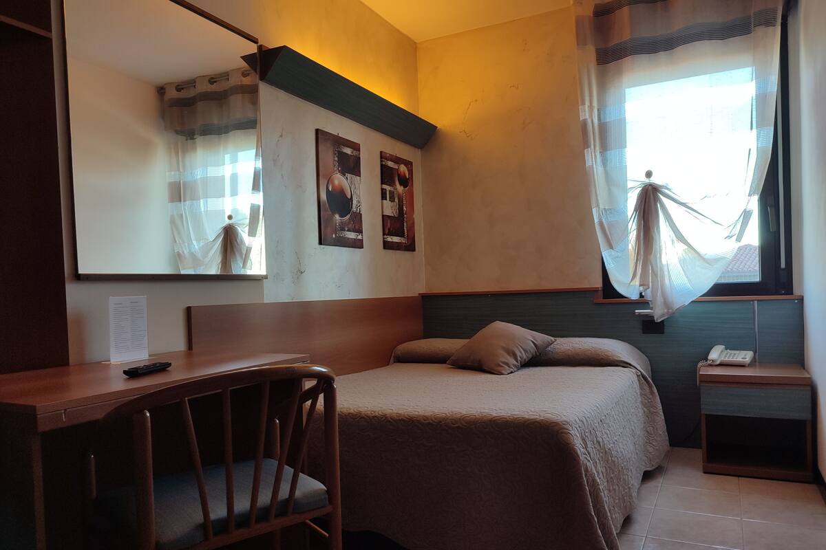 Una habitación de hotel con una cama, un escritorio, una silla, un teléfono y una ventana con cortinas.