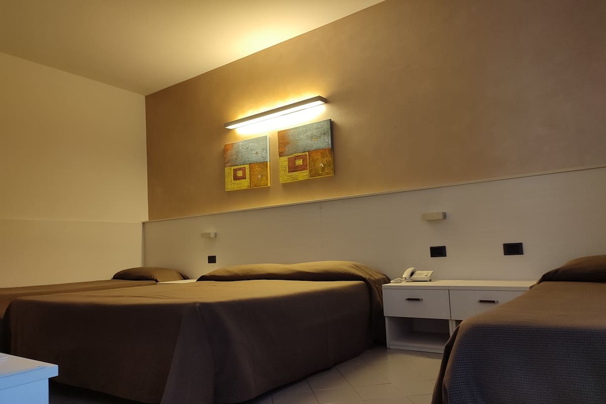 Habitación de hotel con dos camas, una mesita de noche con teléfono y una lámpara fijada a la pared.