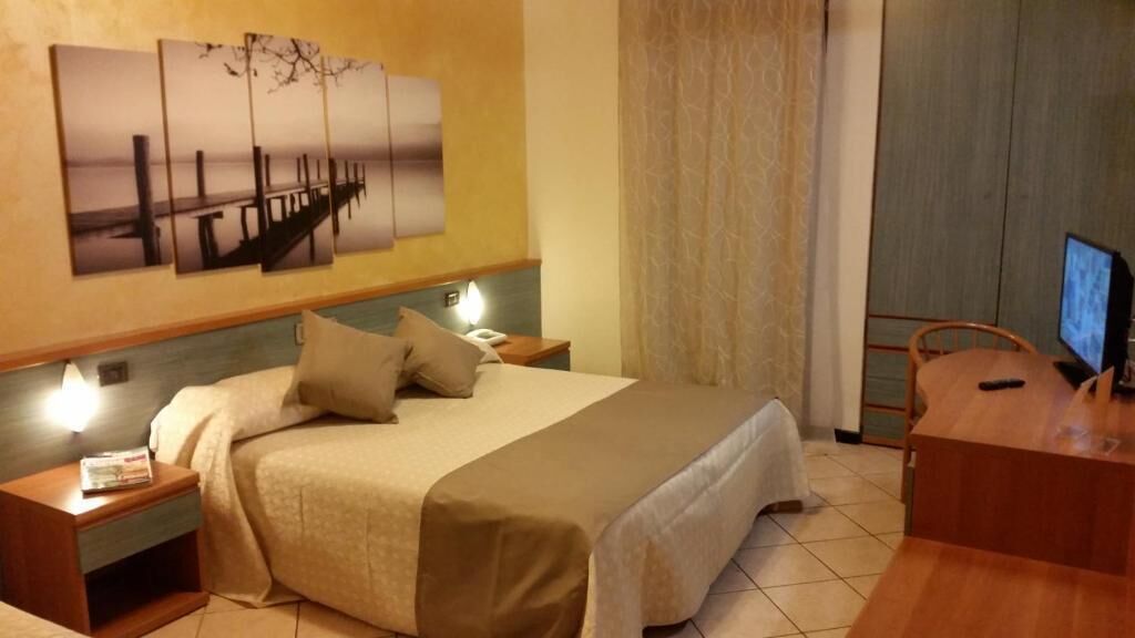 A hotel room with a bed, bedside tables, a desk, a chair, and a wall-mounted TV.
