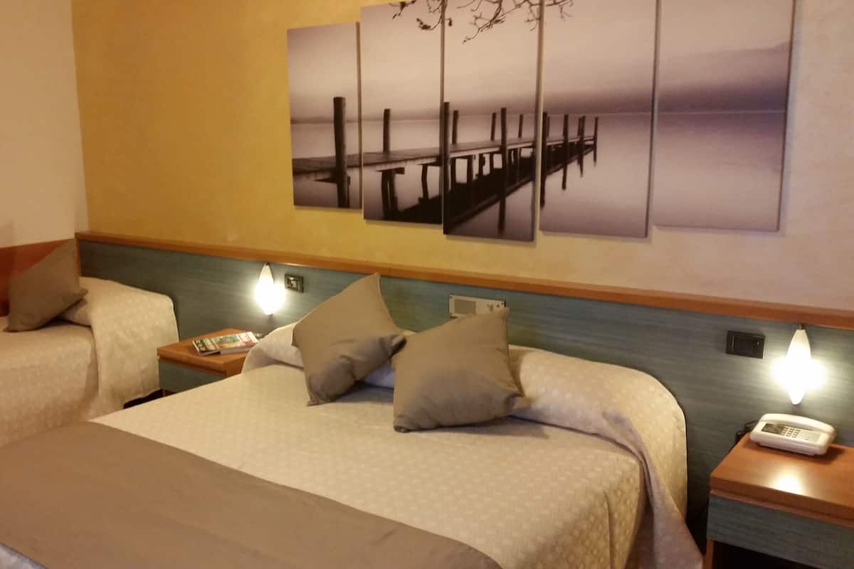 Habitación de hotel con dos camas, una mesita de noche con teléfono y una lámpara fijada a la pared.