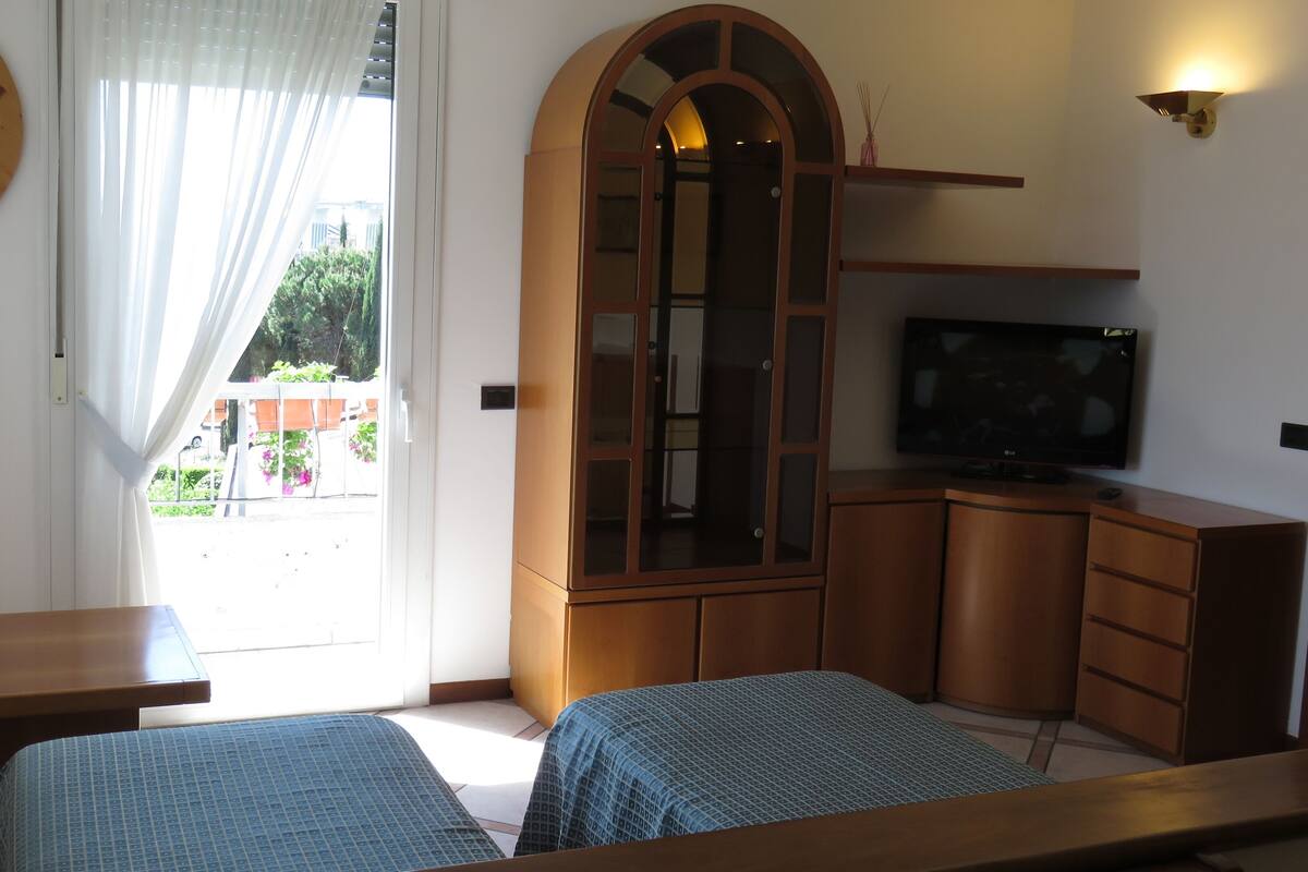 Una habitación con dos camas, televisor, armario de madera y ventana con cortinas.
