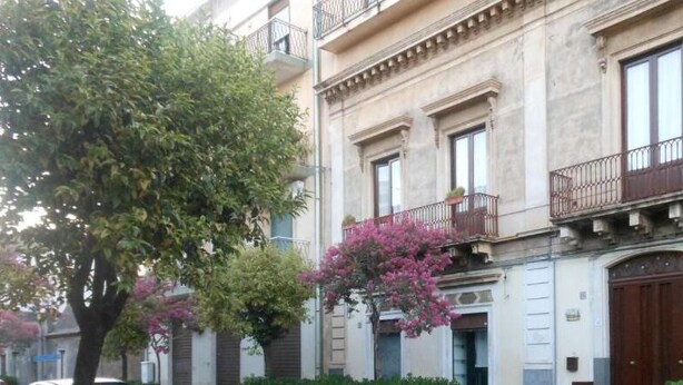 A building with a classic architectural style, featuring a balcony with a wrought iron railing, a large wooden door, and a window with a shutter. - Etna Bed & Breakfast (Belpasso)