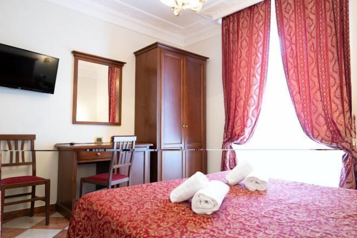 A hotel room with a bed, a desk, a chair, a television, and a wardrobe.