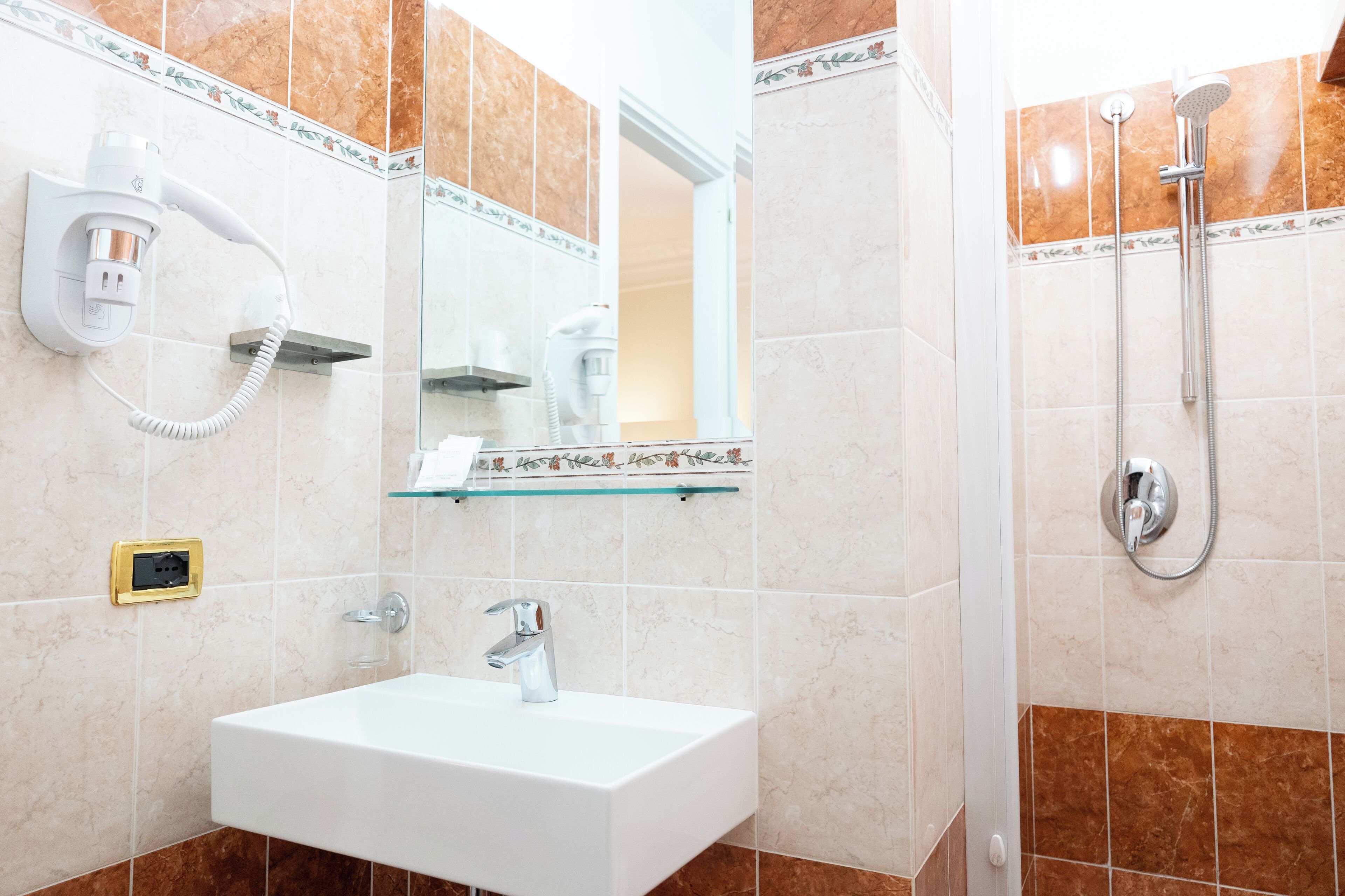 Ein Badezimmer mit Waschbecken, Spiegel, Föhn und Dusche.