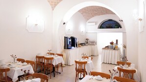 A dining area with tables set for meals, a coffee machine, and a view through an arched doorway. - Hotel RomAntica (Rome)