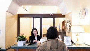 A reception desk with a clock, a sign indicating WiFi availability, and a potted plant. - Hotel RomAntica (Rome)