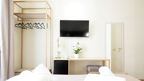 A hotel room with a bed, a desk with a TV, a wardrobe, a small plant, and a door. - Hotel RomAntica (Rome)
