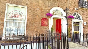 A brick building with a red door, a sign for Bagshot Court Towhouse, and a window with a curtain. - Baggot Court Townhouse (Dublin)