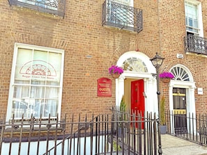 A brick building with a red door, a sign for Bagshot Court Towhouse, and a window with a curtain. - Baggot Court Townhouse (Dublin)