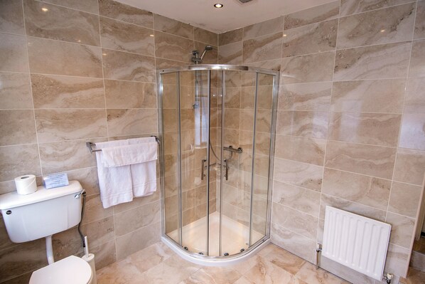A modern bathroom with a glass-enclosed shower, beige marble tiles, a toilet, and a white radiator. - Baggot Court Townhouse (Dublin)
