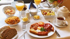 A breakfast table with various dishes including toast, beans, tomatoes, and sausages. There are also glasses of orange juice and a fruit basket. - Baggot Court Townhouse (Dublin)
